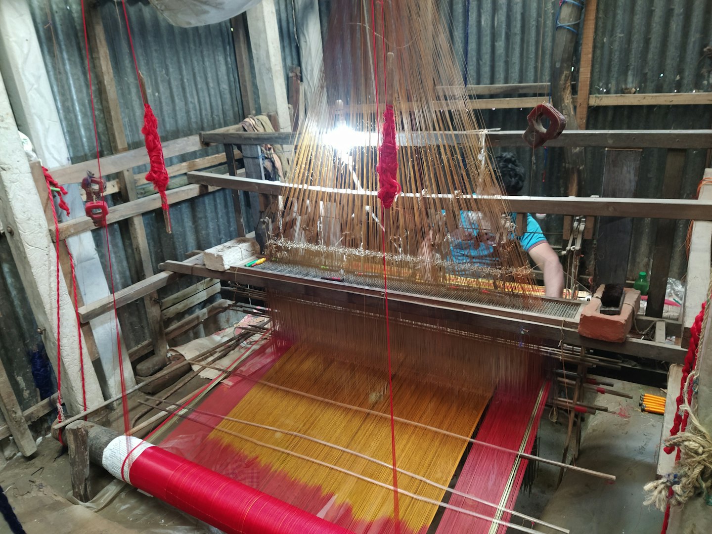 Artisan weaving red and gold fabric on a wooden loom.
