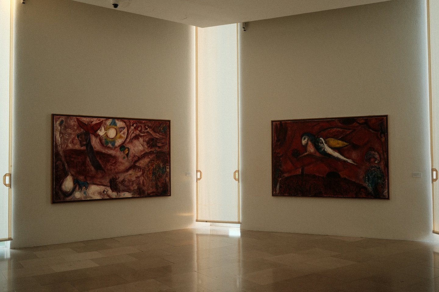 Two abstract paintings hang on gallery walls above tiled floors.